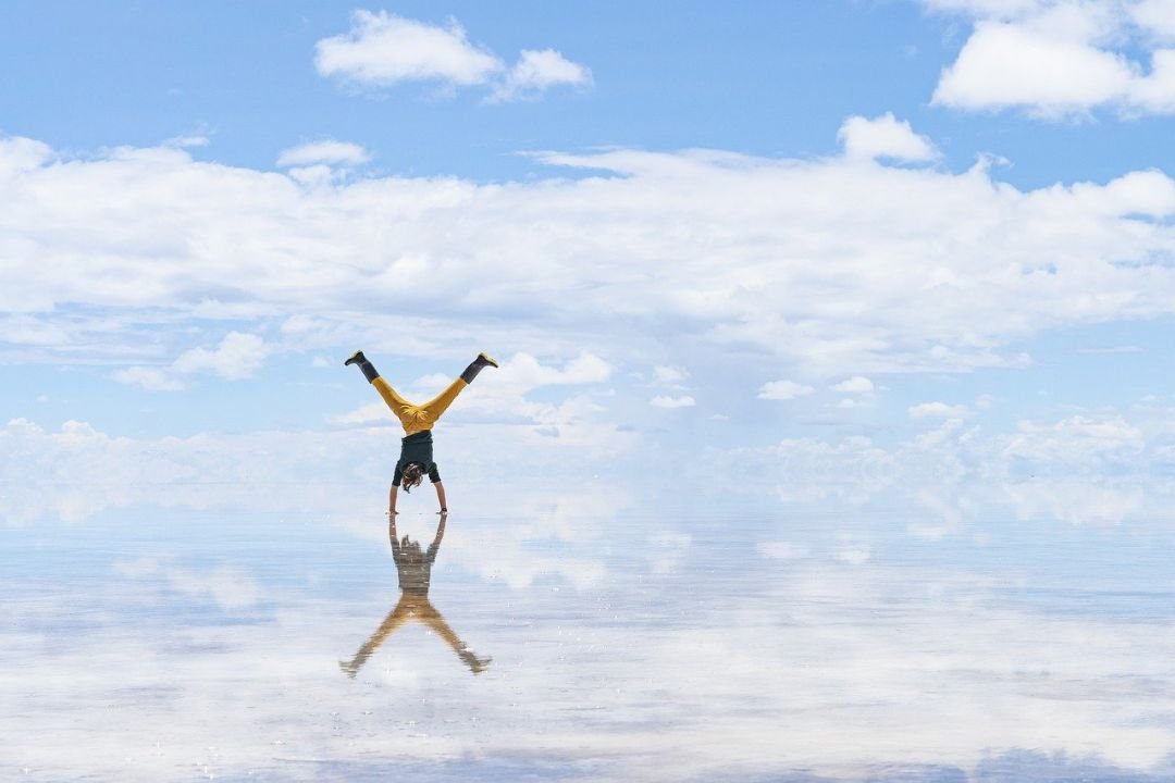 imagen de un turista jugando con el efecto reflejo de el salar de uyuni en temporada de lluvia, no se diferencia la linea que divide el cielo del suelo.