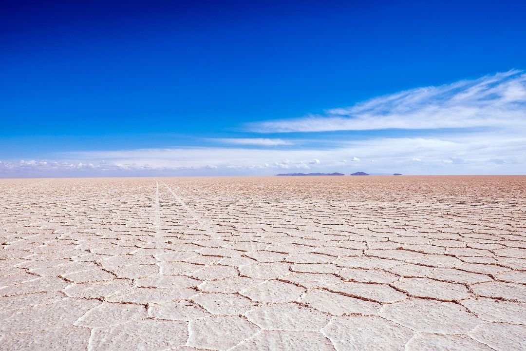 imagen de el salar de uyuni con su tradicional forma de la sal en hexagonos y de fondo a lo lejos una isla en medio.