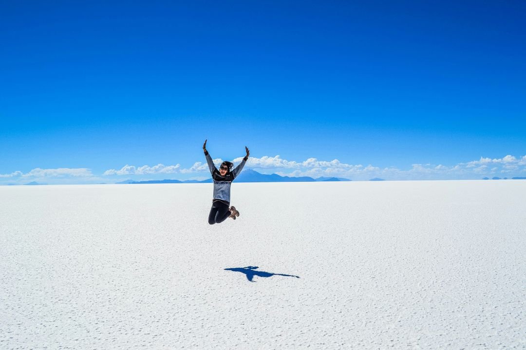 imagen de un turista en pleno salar de Uyuni y de fondo unas montañas con nubes en un dia soleado.