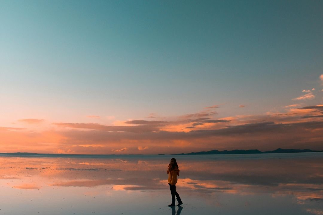 imagen de atardecer con una turista en medio de la inmensidad de el Salar de Uyuni.