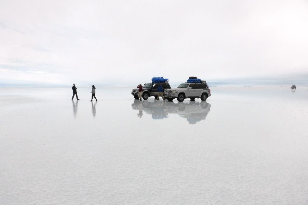 imagen de turistas en el Salar de Uyuni, con sus vehiculos y la bastedad de fondo.